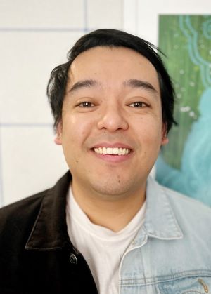 headshot of a person wearing a black and blue button up shirt in front of a white backdrop